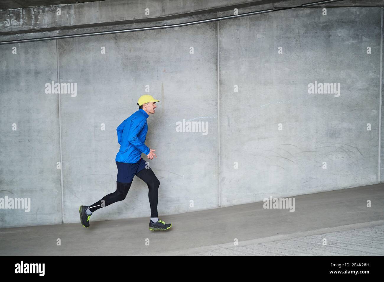 Lächelnder reifer Mann beim Joggen an der grauen Wand in der Parkgarage Stockfoto