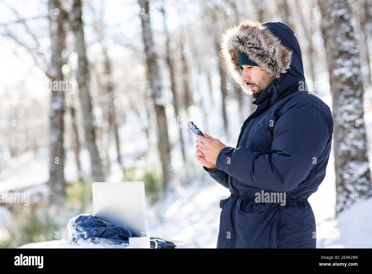 Männlicher Profi in warmer Kleidung mit Smartphone im Schnee Stockfoto