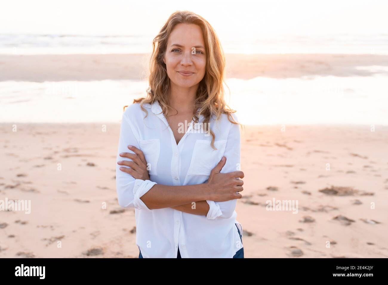 Lächelnde Frau, die mit gekreuzten Armen am Strand steht Stockfoto