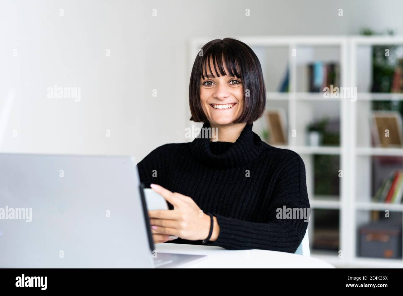 Glückliche junge Frau mit Laptop im Arbeitszimmer Stockfoto
