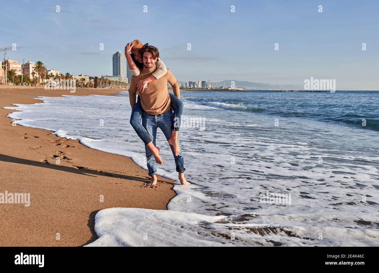 Mann Huckepack verspielte Frau, während am Strand stehen Stockfoto