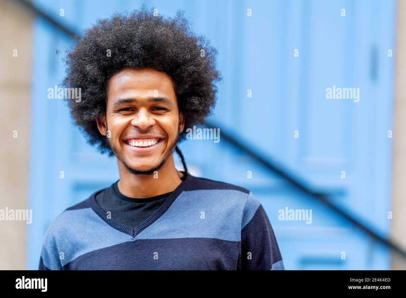 Nahaufnahme eines lächelnden jungen Mannes mit lockigen Haaren an der Wand Stockfoto