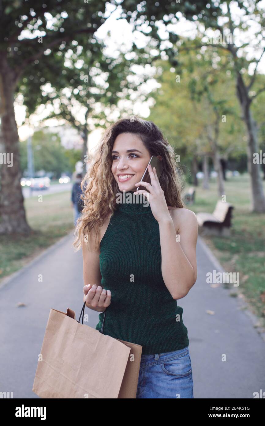 Lächelnde Frau, die wegschaut, während sie beim Telefonieren anruft Öffentlicher Park Stockfoto