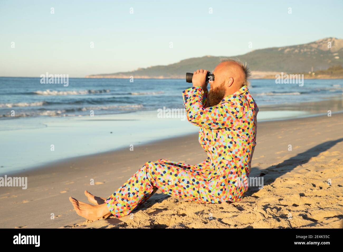Mann trägt bunten Anzug mit binokular, während am Strand sitzen Stockfoto
