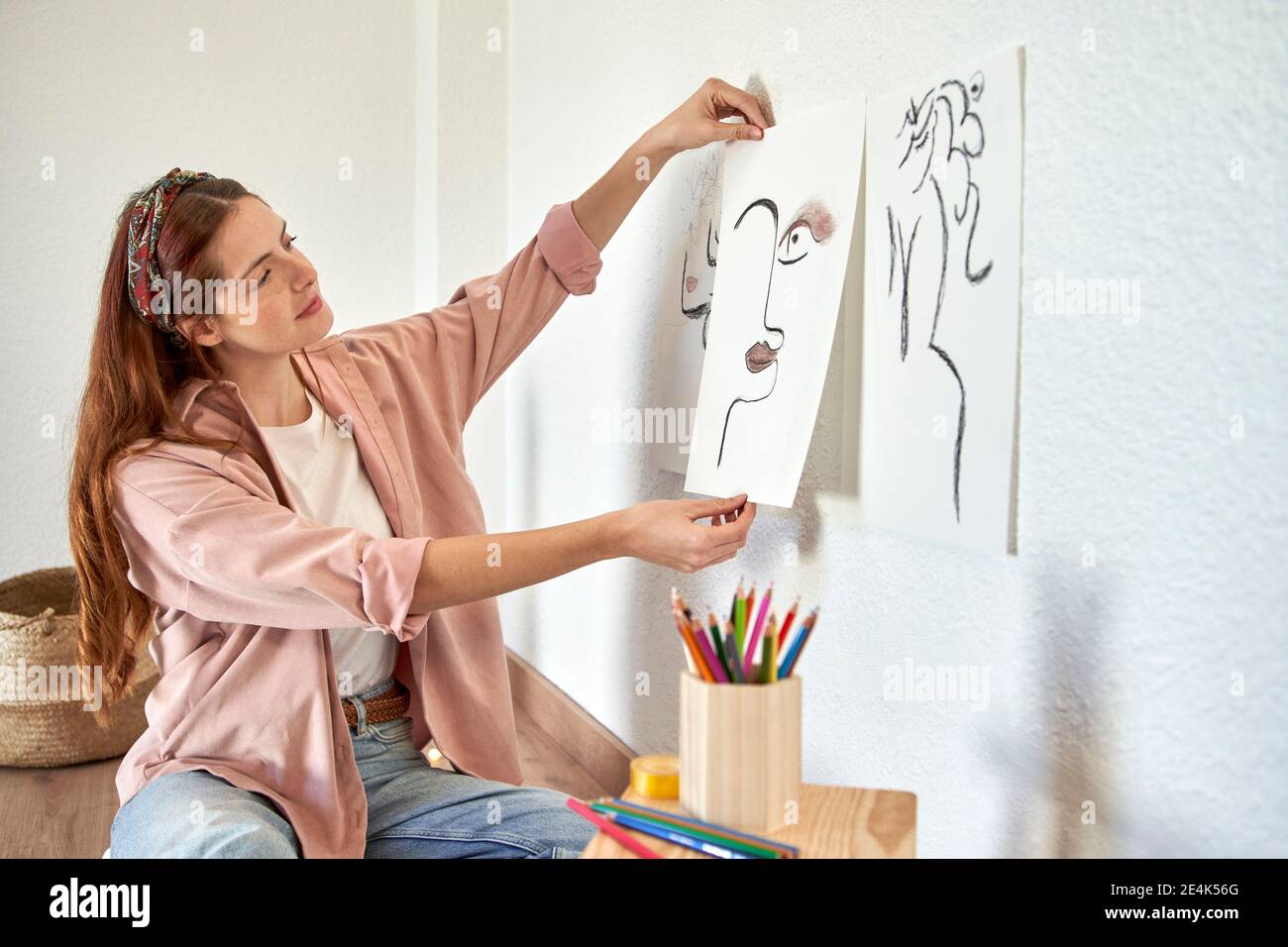 Weibliche Künstlerin, die Kohlezeichnung an die Wand im Wohnzimmer kleben Stockfoto