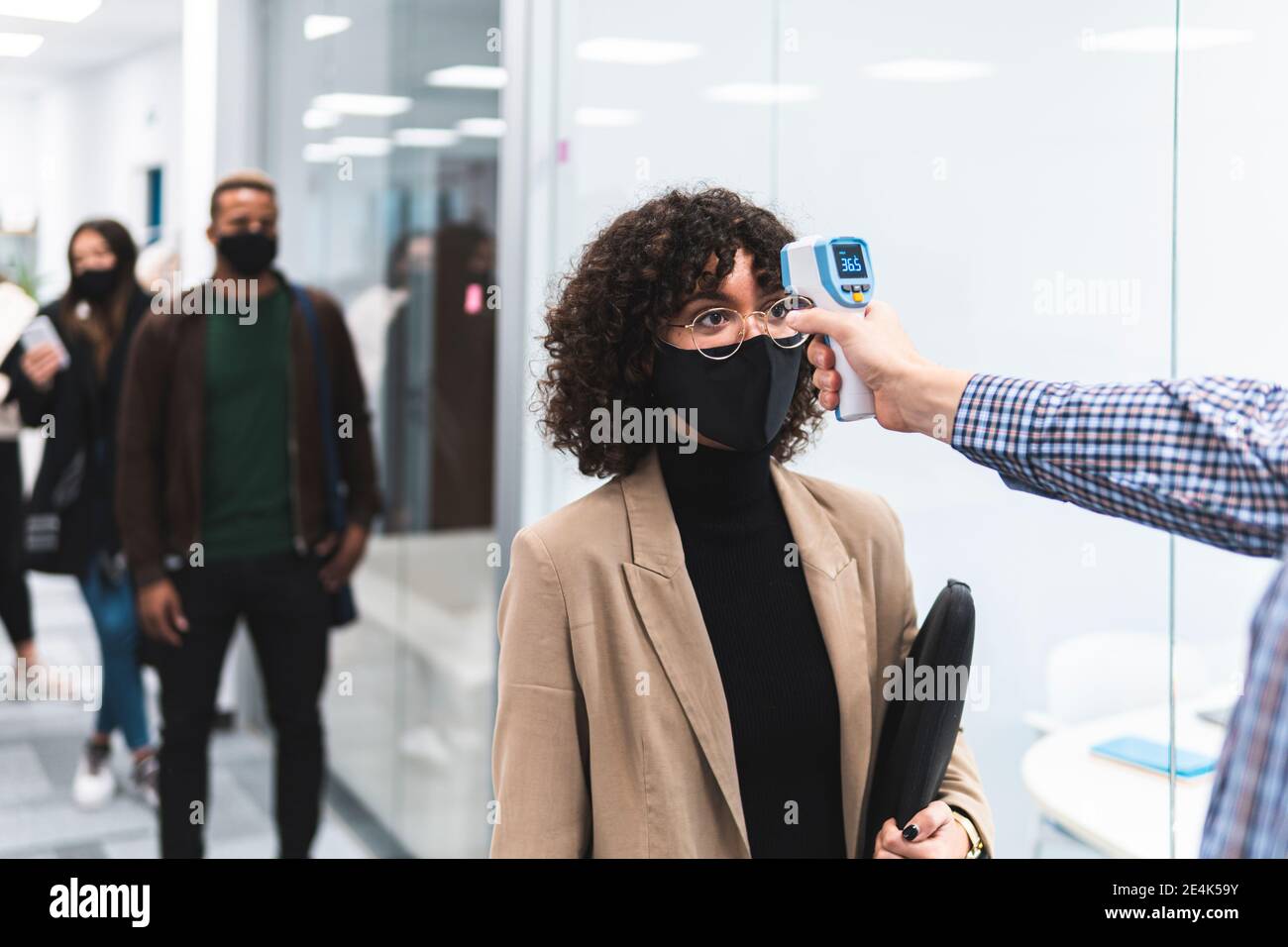 Weibliche professionelle geht durch Temperaturkontrolle, bevor sie zur Arbeit gehen Im Büro Stockfoto