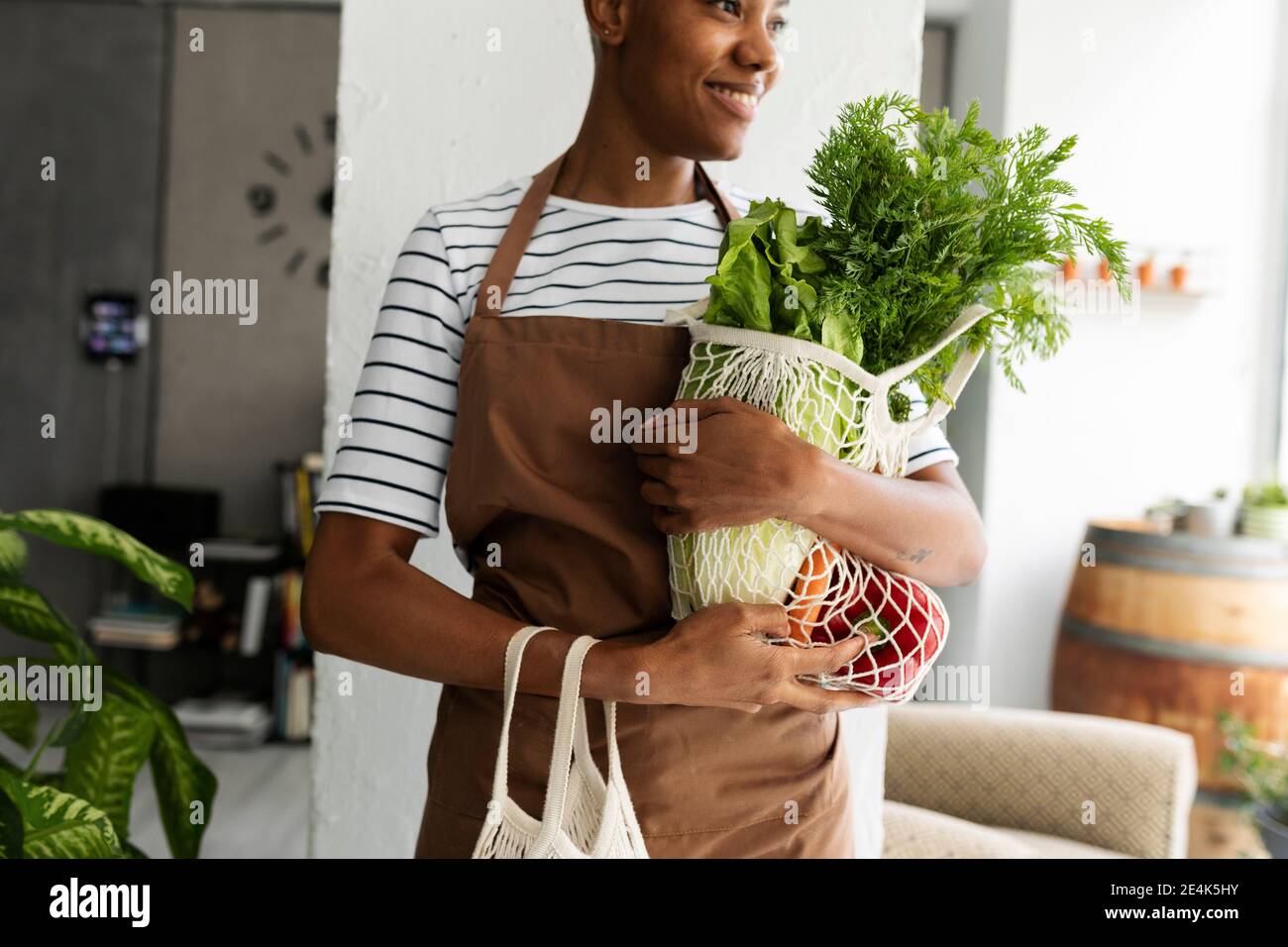 Hübsche Frau in Schürze, die Netz mit frischem Gemüse trägt Stockfoto