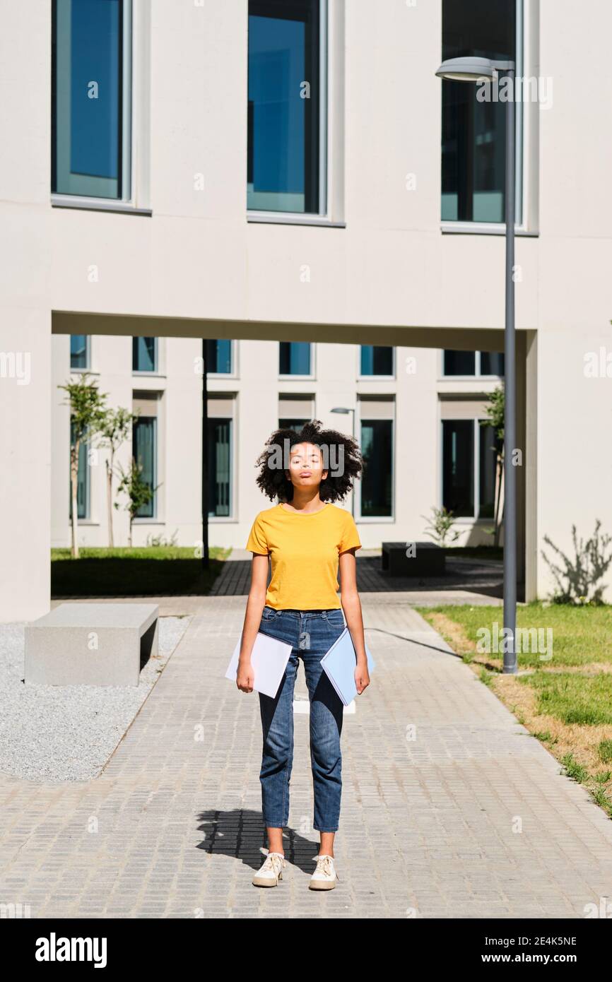 Junge Studentin, die Bücher hält, während sie mit geschlossenen Augen steht universität Stockfoto