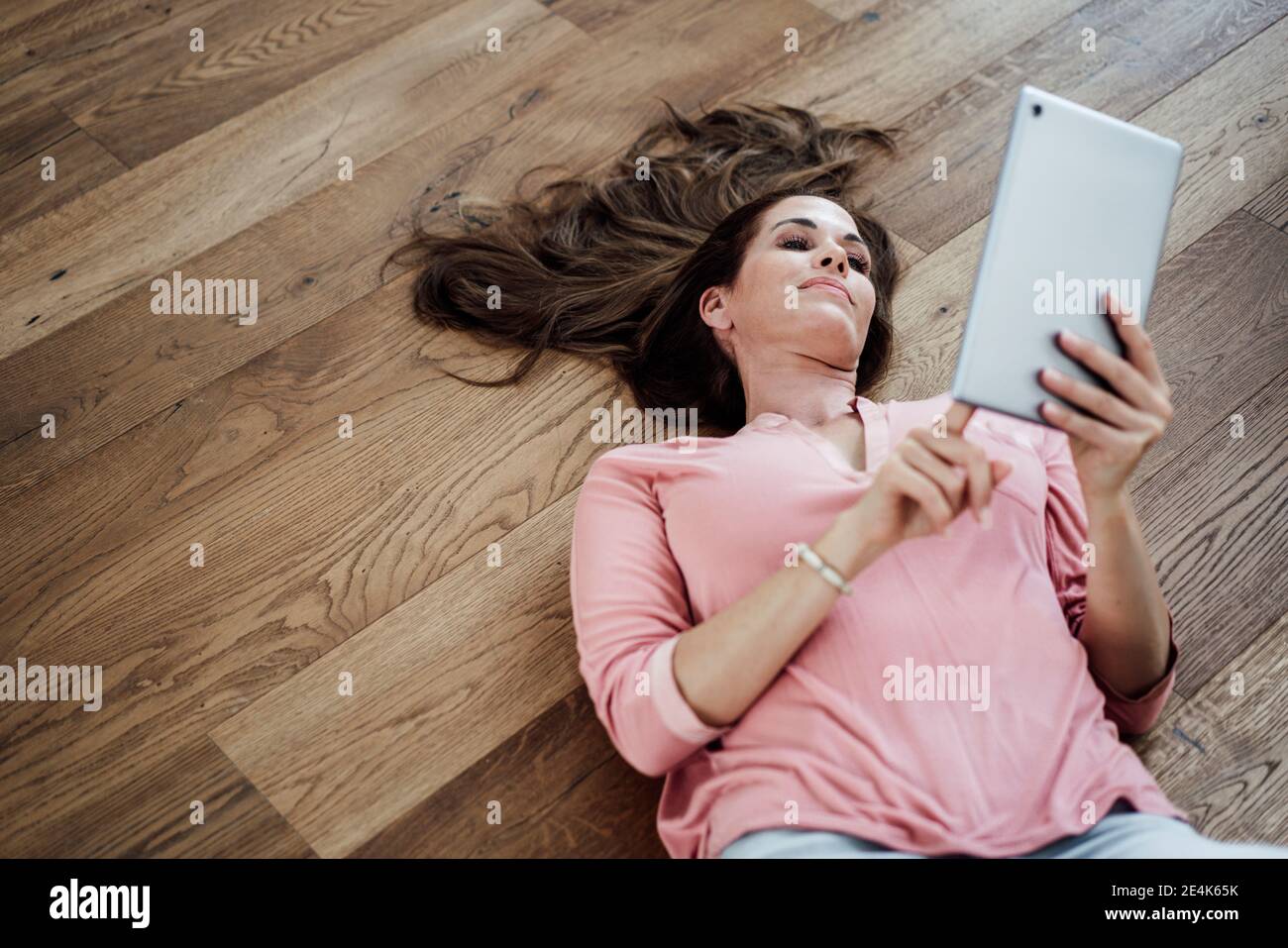 Reife Frau mit digitalen Tablet, während auf dem Boden liegen in Wohnung Stockfoto