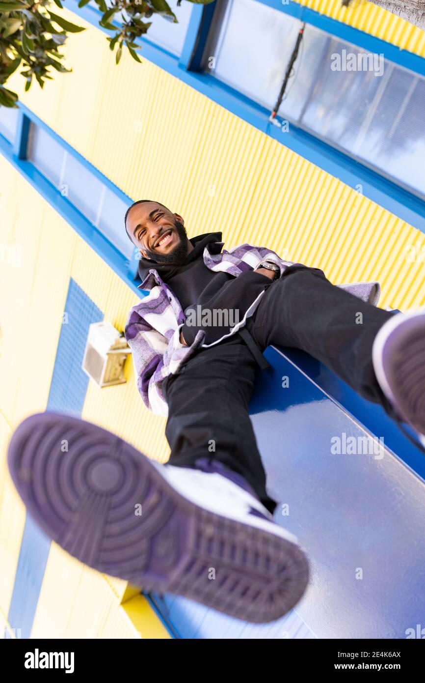 Fröhlicher junger Mann mit Händen in Taschen gegen gelbes Gebäude Außen Stockfoto