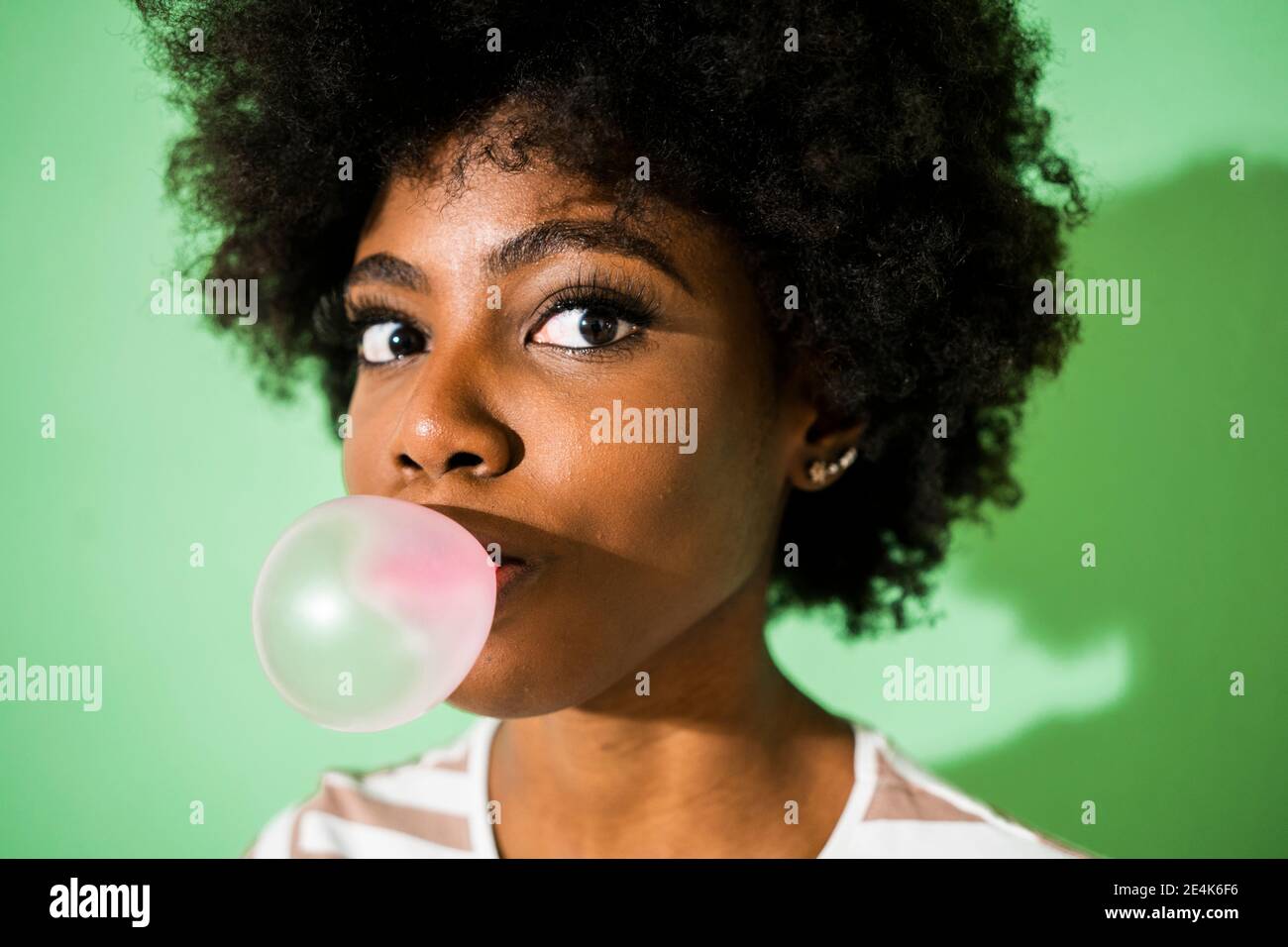 Junge Frau bläst Blase Gummi, während vor grünem Hintergrund stehen Stockfoto