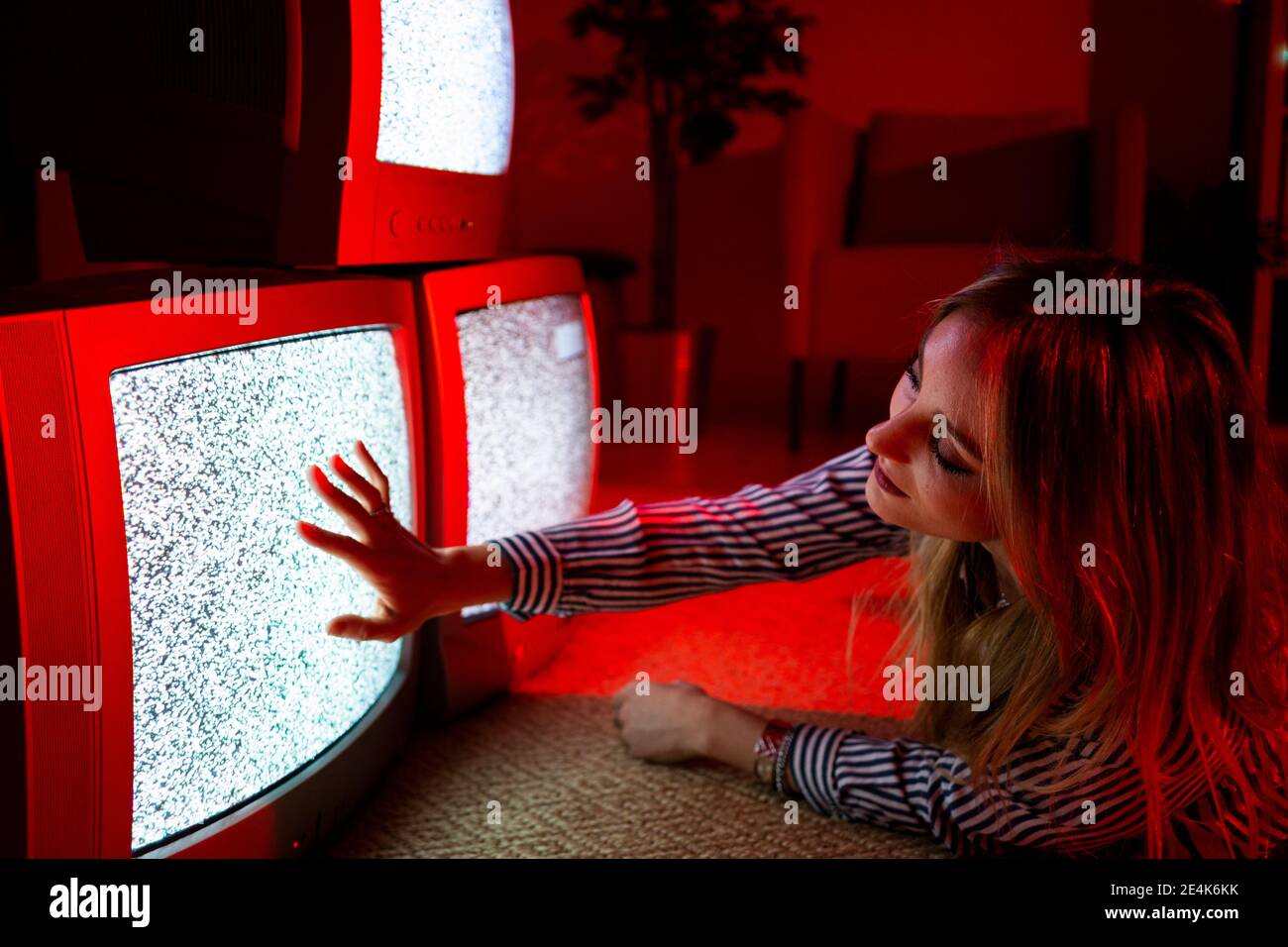 Junge Frau berührt Vintage-TV-Bildschirm, während auf der Vorderseite liegen Zu Hause Stockfoto