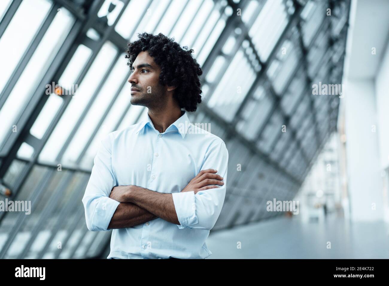 Nachdenkliche junge männliche professionelle stehend mit Armen gekreuzt, während suchen Unterwegs am Arbeitsplatz Stockfoto