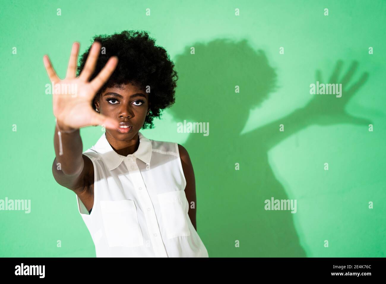 Lockiges Haar Frau zeigt Stop-Geste, während sie gegen grün steht Hintergrund Stockfoto