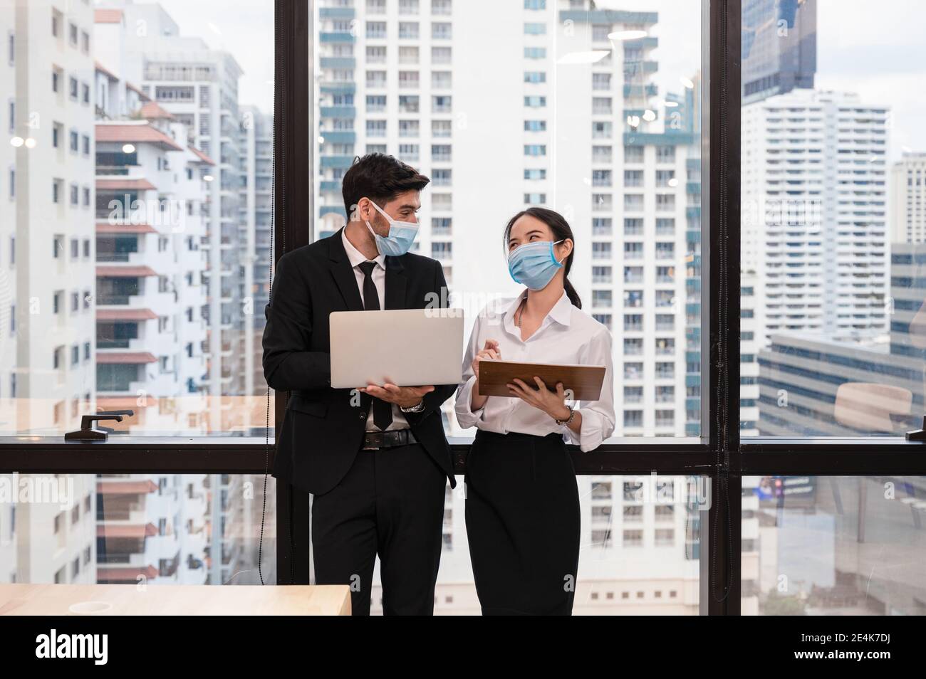 Multiethnische Geschäftskollegen tragen Gesichtsmaske und lächeln mit Diskussion in neuen normalen Büro im Geschäftsviertel. Während Pandemie des Coronavirus Stockfoto