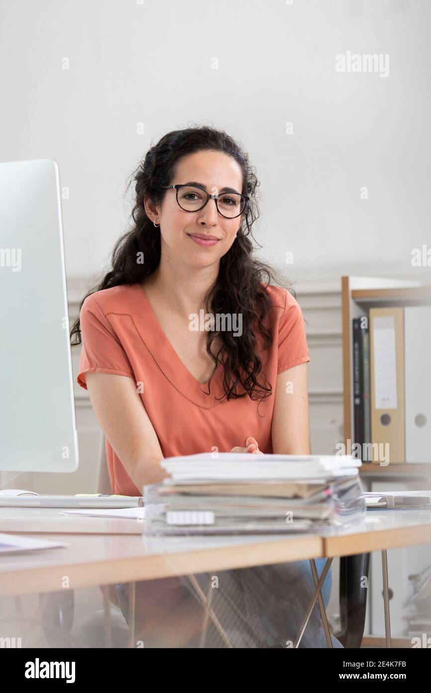 Weibliche professionelle lächelnd, während sie am Schreibtisch im Büro sitzt Stockfoto Weibliche professionelle lächelnd, während sie am Schreibtisch im Büro sitzt Stockfoto