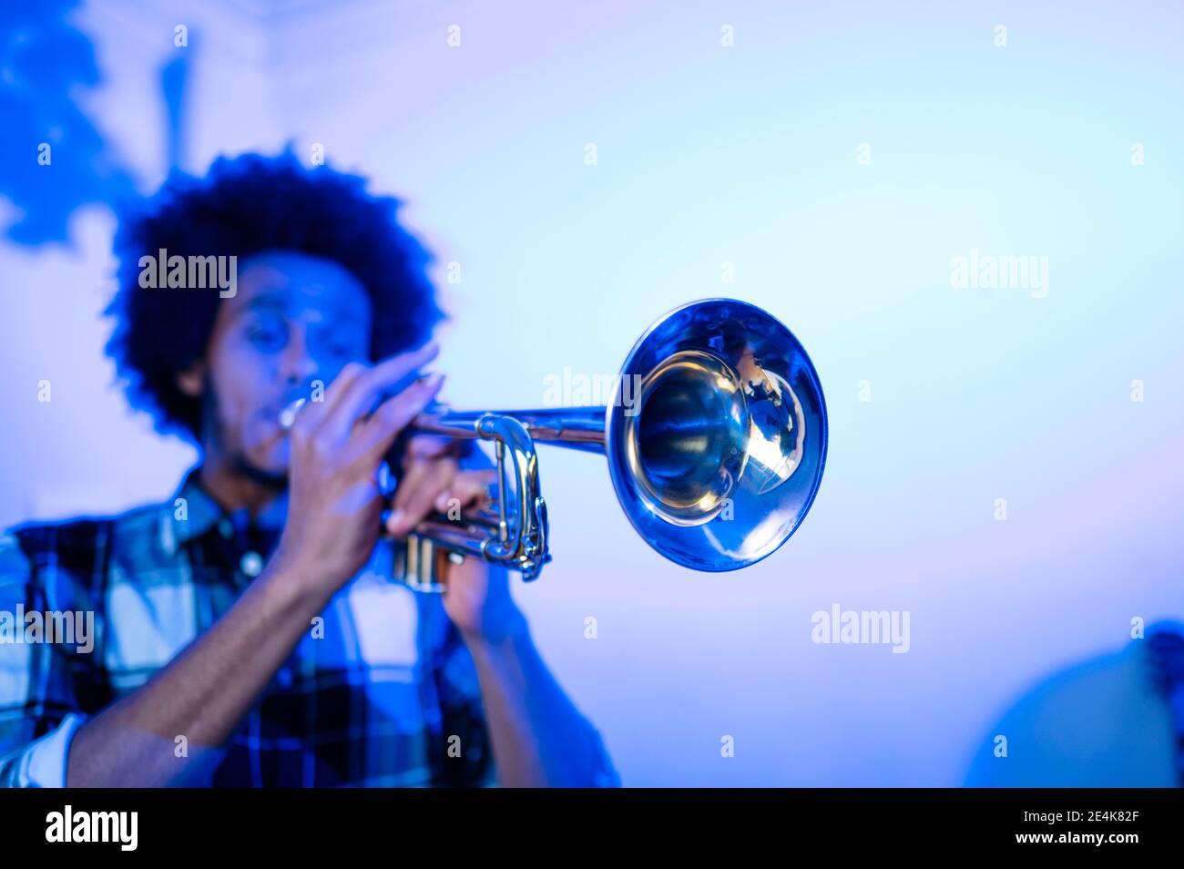 Junger Musiker, der im blauen Raum Trompete an der Wand übt Stockfoto