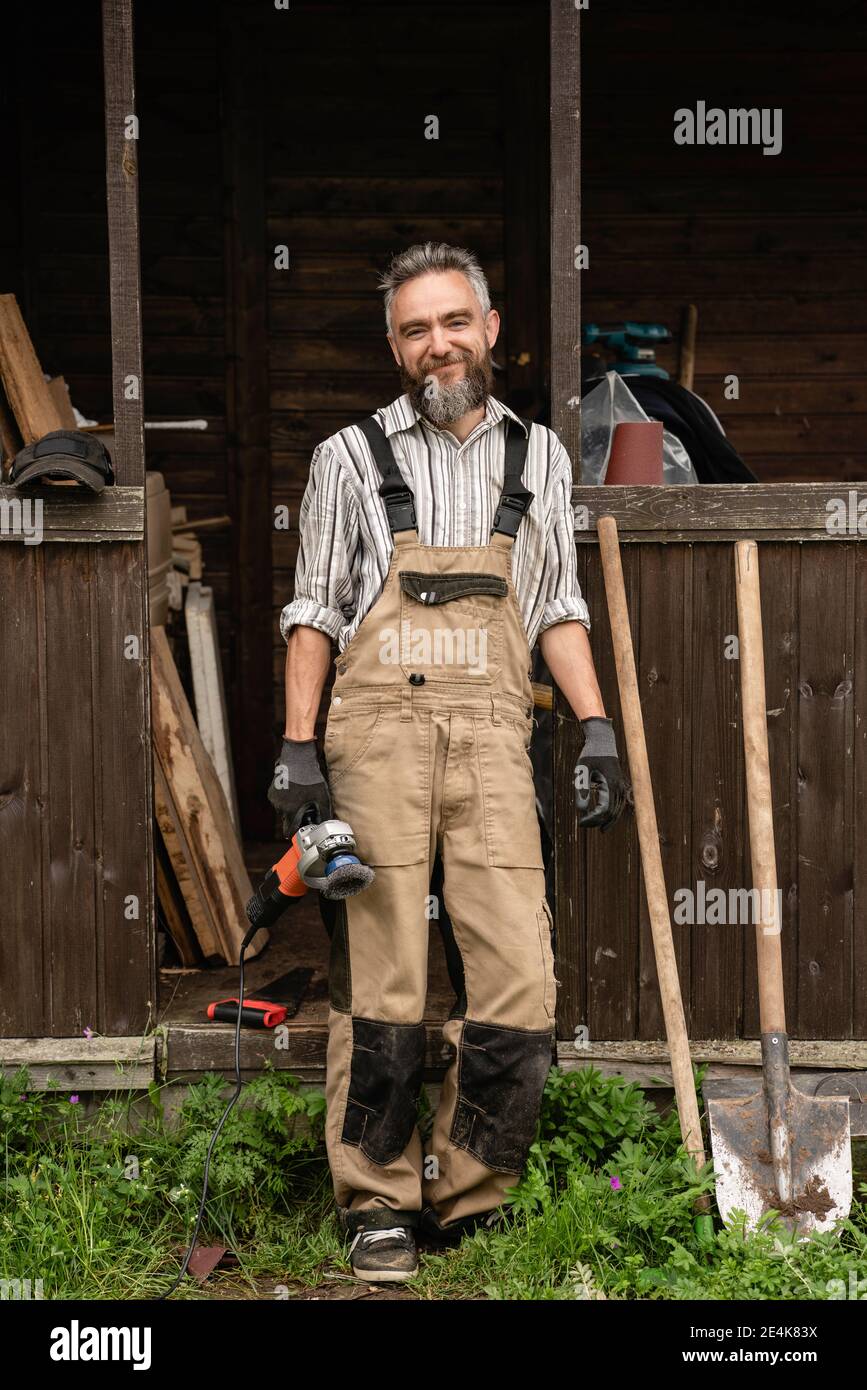 Porträt eines bärtigen Zimmermanns, der im Freien steht, mit Mühle in der Hand Stockfoto