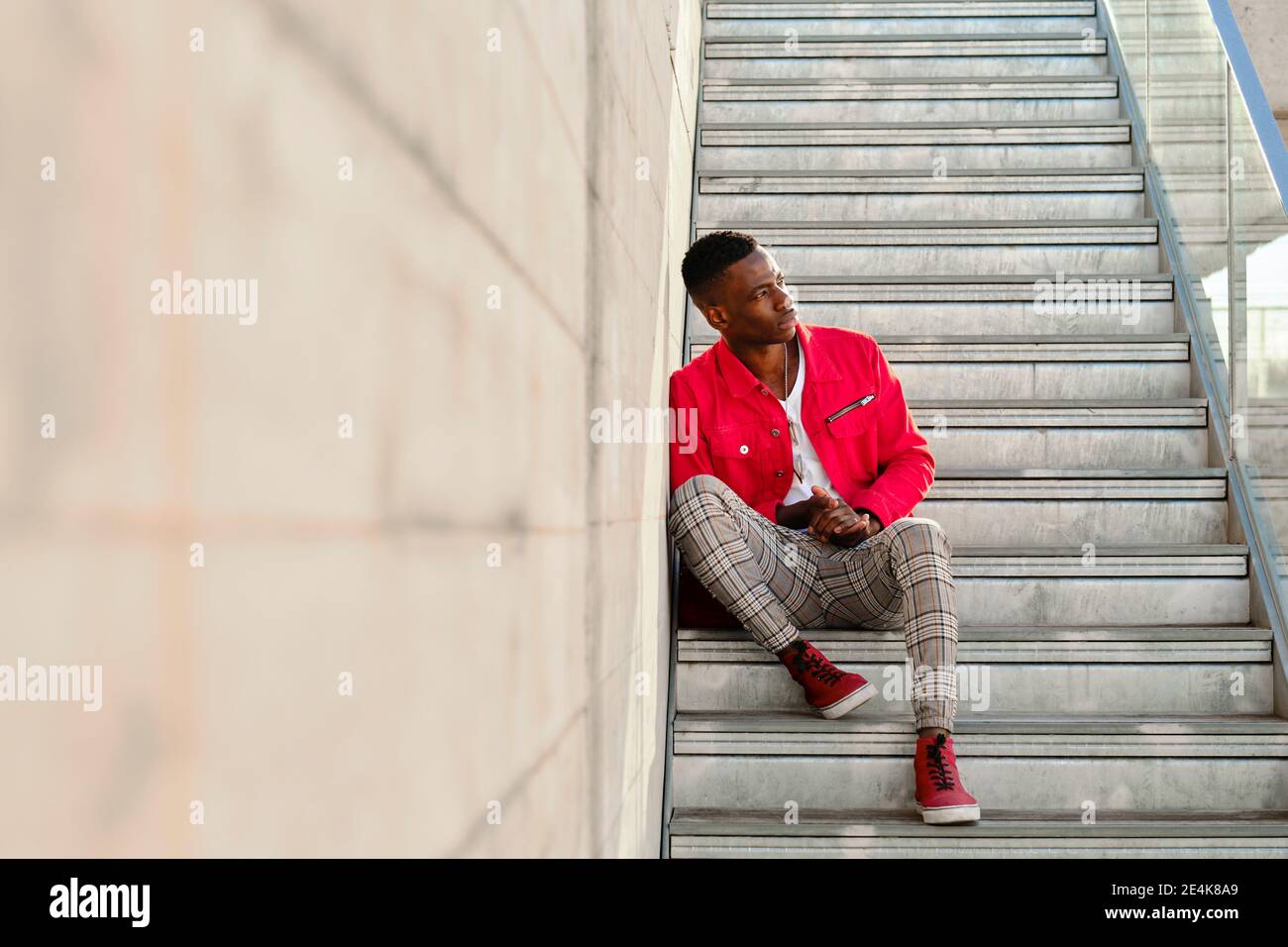 Junger Mann in roter Jacke und karierter Hose sitzend Tritt im Freien auf Stockfoto