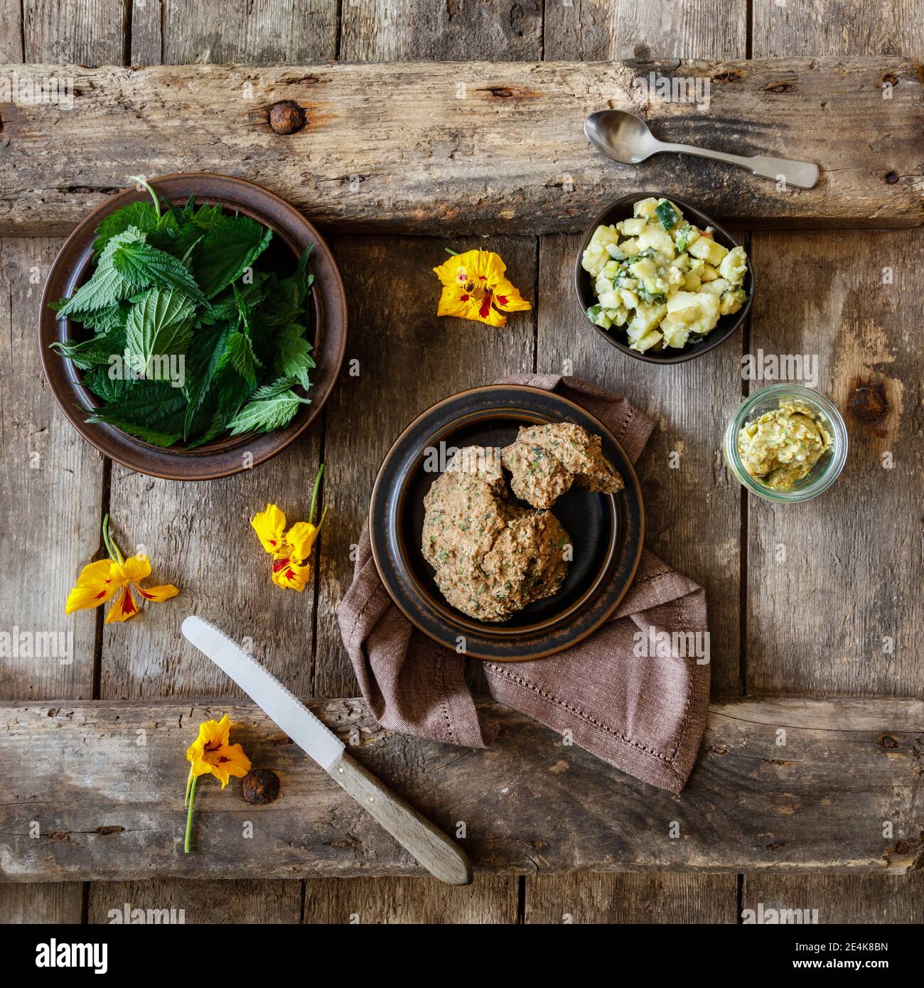 Kartoffelsalat, frische Brennnessel, Kräuterbutter und gelbe Blütenköpfe Stockfoto