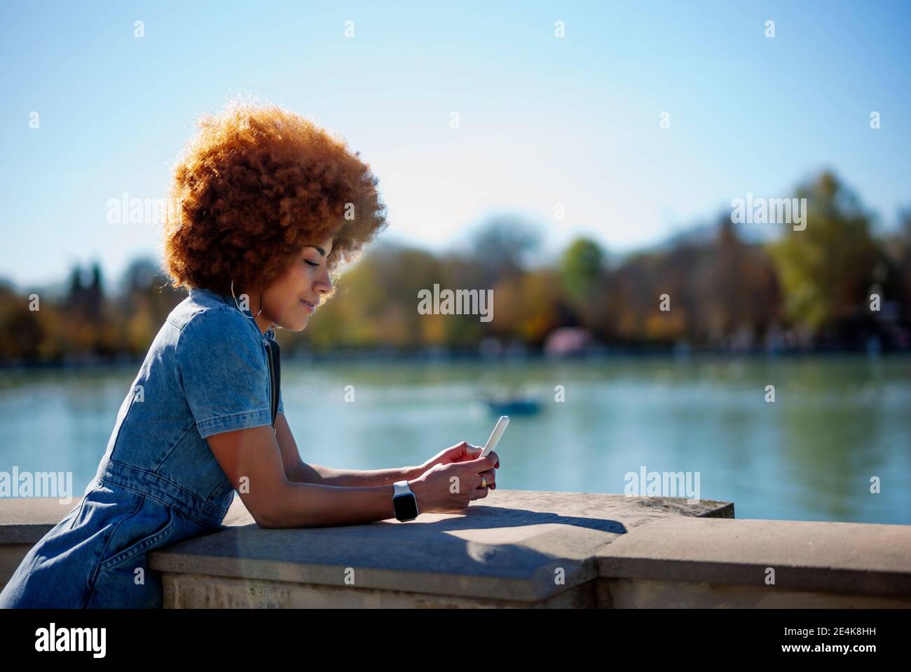 Mittlere Erwachsene Frau mit krausem Haar mit Handy in Estanque Grande Del Retiro Teich an sonnigen Tag, Spanien Stockfoto