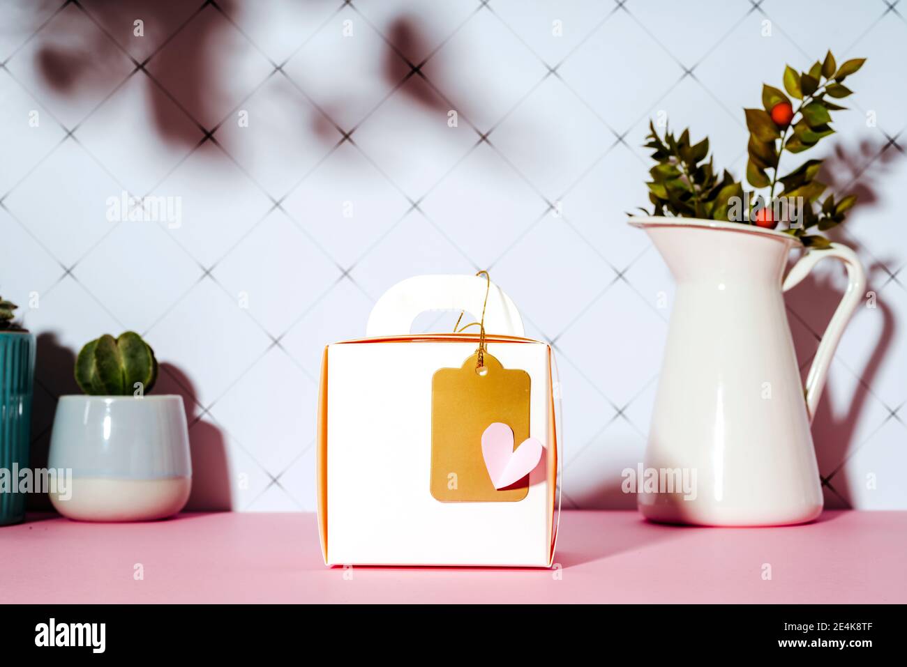 Geschenkschachtel mit goldenem Etikett und einem Papierherz auf Rosa Tisch von Pflanzen Stockfoto