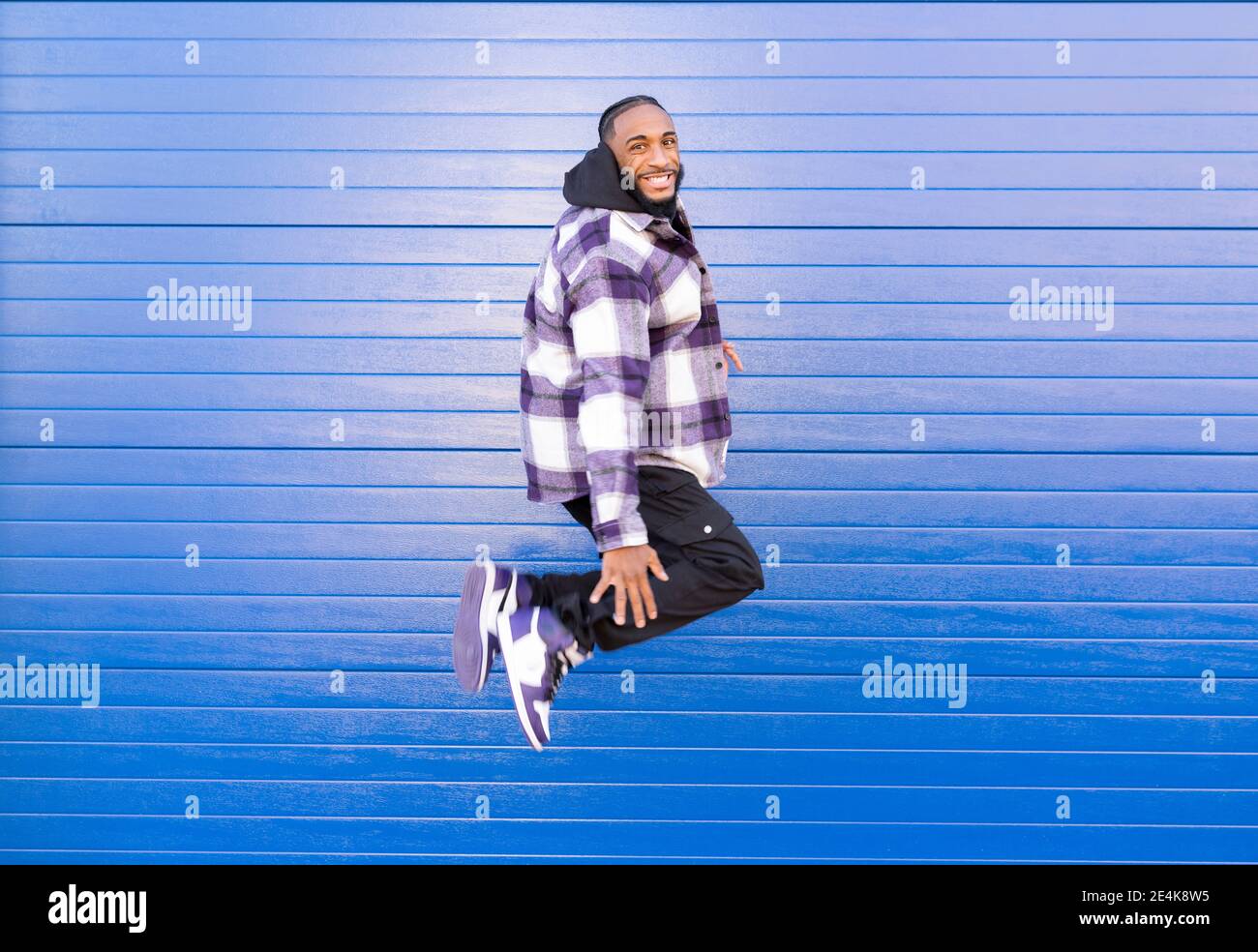 Glücklicher junger Mann in der Luft gegen blaues Wellblech Stockfoto