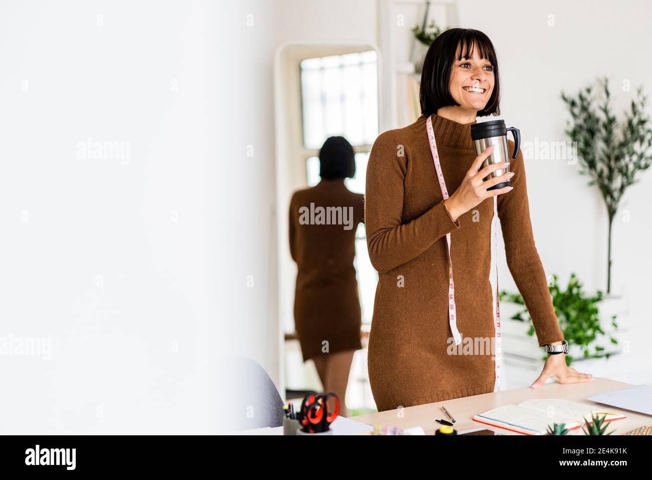 Glücklich junge Frau Stylistin Tag träumen, während Kaffee Tasse halten Im Atelier Stockfoto