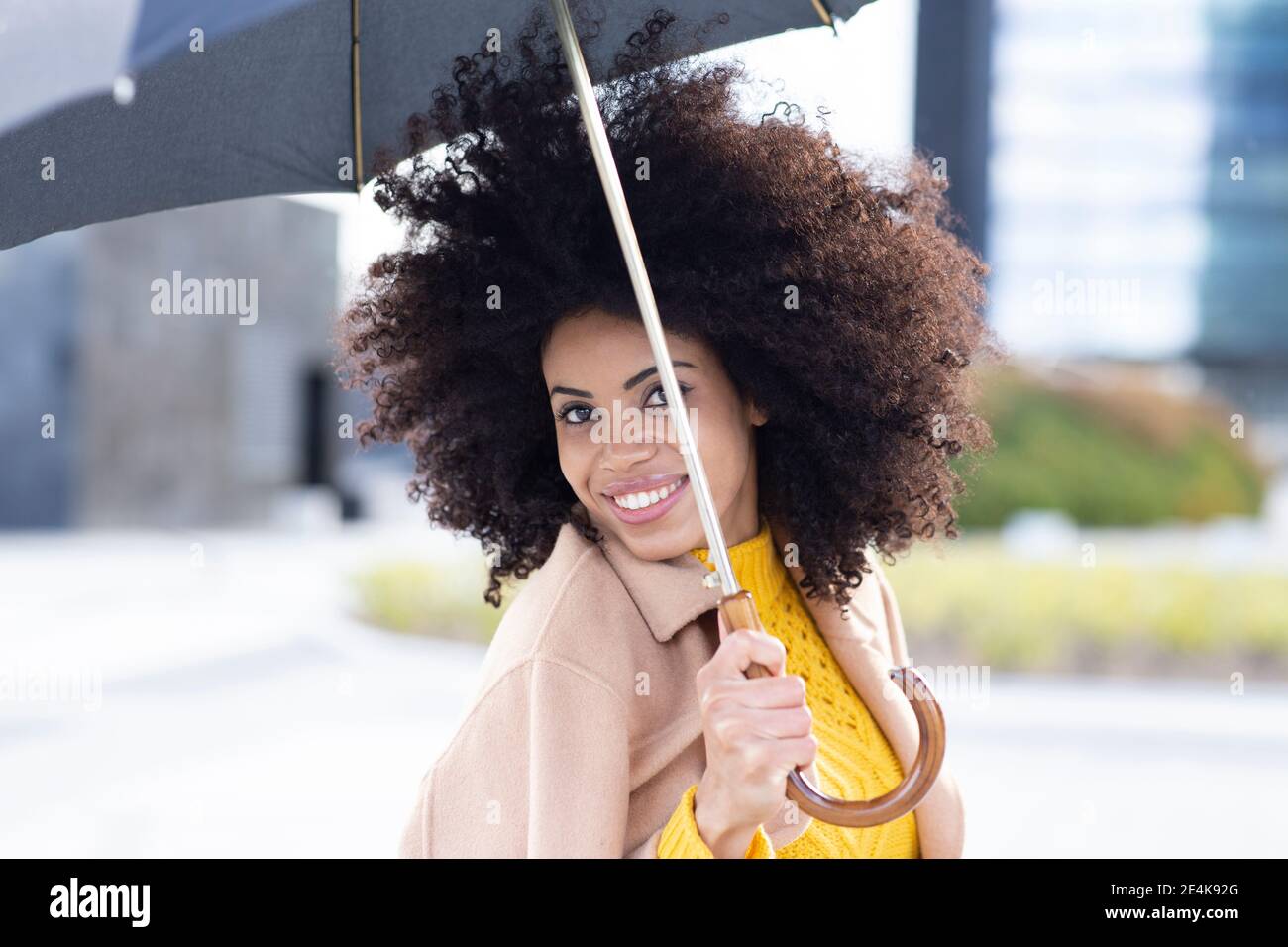 Junge Frau lächelt, während sie den Regenschirm im Freien hält Stockfoto