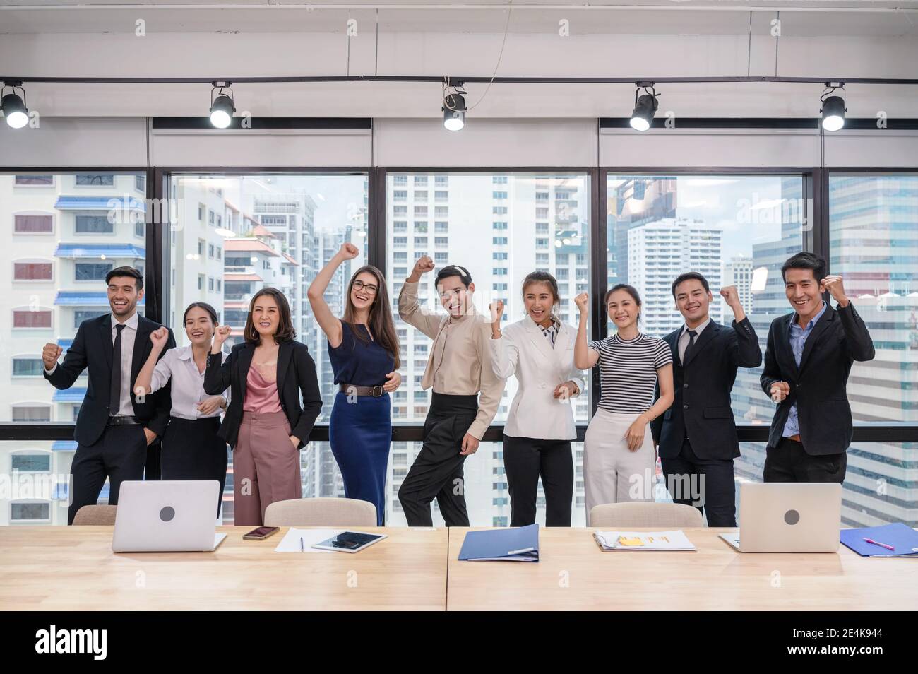 Multi ethnischen Business-Team feiert der erfolgreiche in modernen Büro im Geschäftsviertel. Geschäftsleute stehen in einer Reihe mit erhobenem Arm Stockfoto
