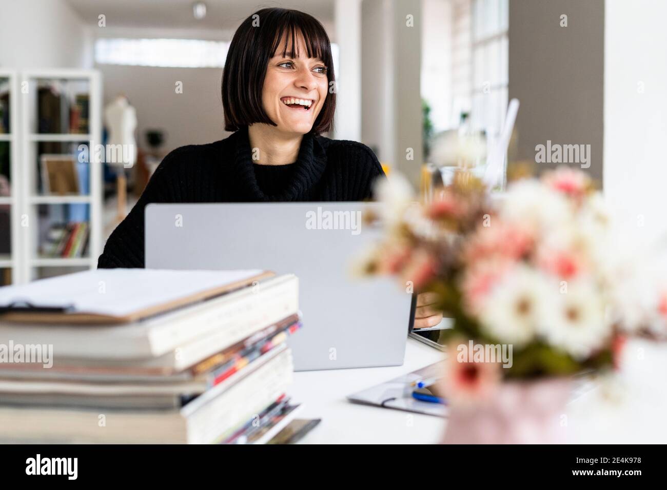 Lächelnder junger Student mit Laptop, der im Arbeitszimmer wegschaut Stockfoto