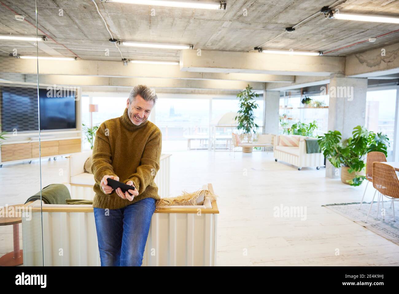 Glücklicher Mann, der Spiel auf dem Handy spielt, während er sitzt Zu Hause Stockfoto