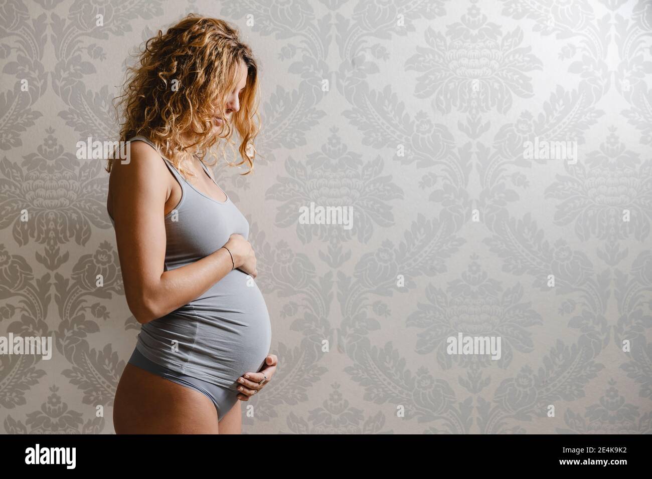 Schwangere Frau mit blondem Haar an der Wand zu Hause Stockfoto