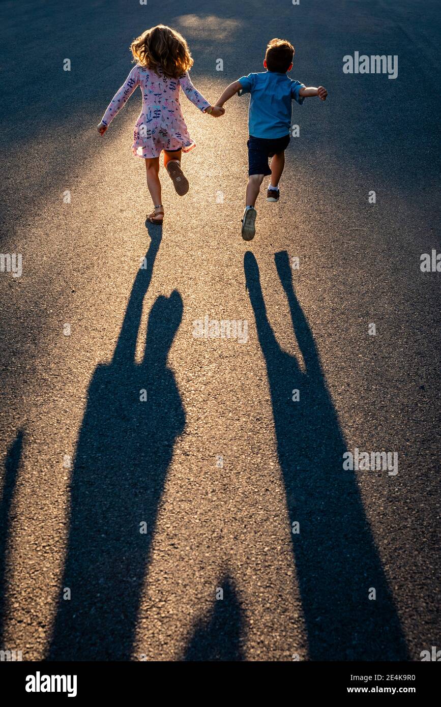 Rückansicht von Geschwistern, die Hände halten und auf der Straße laufen Stockfoto