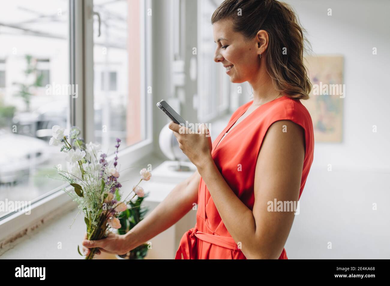 Lächelnde Frau fotografiert Blumen mit Smartphone Stockfoto