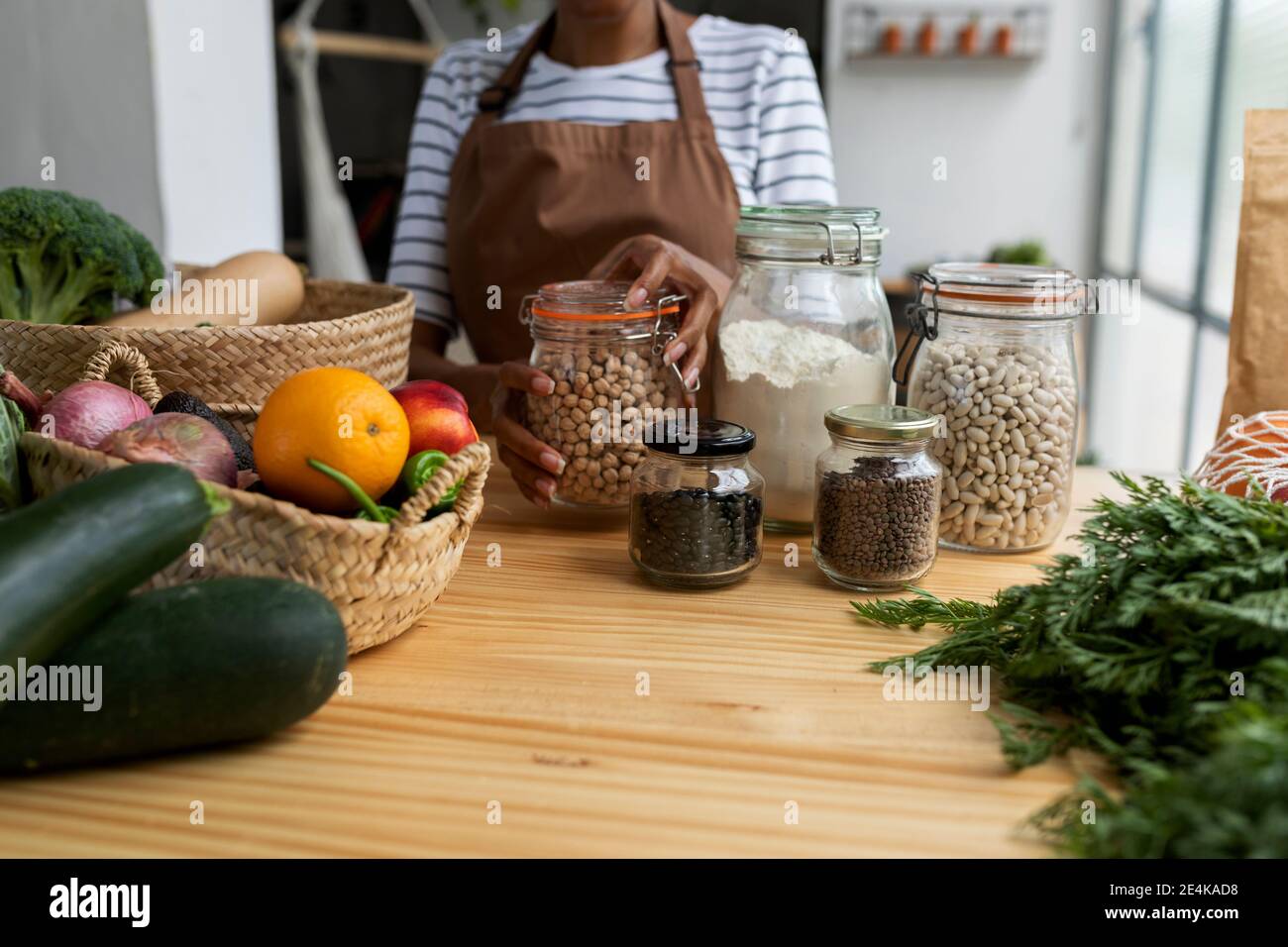 Frau mit Schürze Lagerung Hülsen in Gläsern auf Tisch mit Frisches Obst und Gemüse Stockfoto