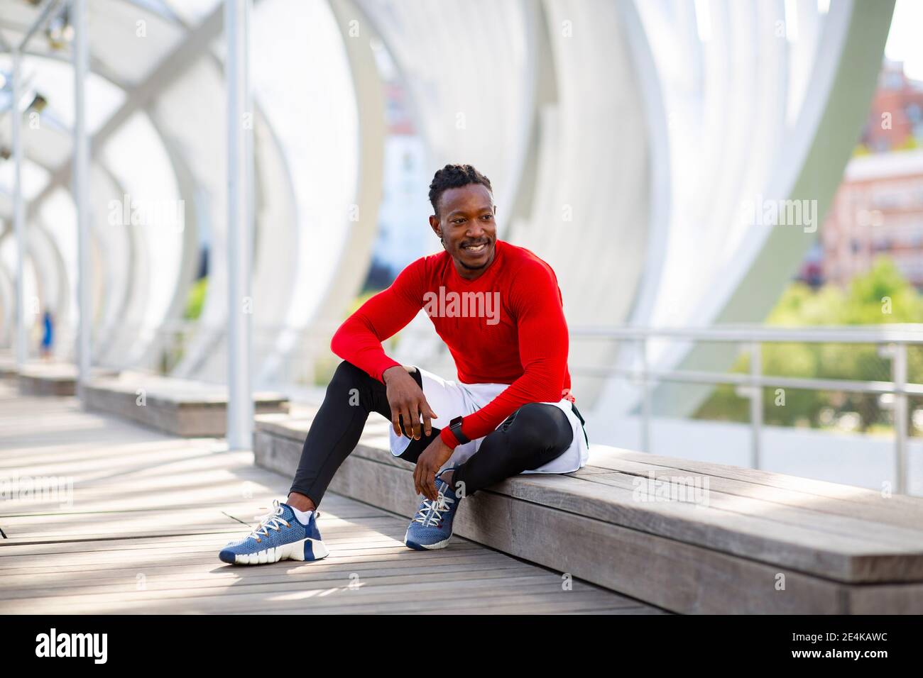 Lächelnder Sportler, der wegschaut, während er sich auf der Laufbank ausruht Stockfoto