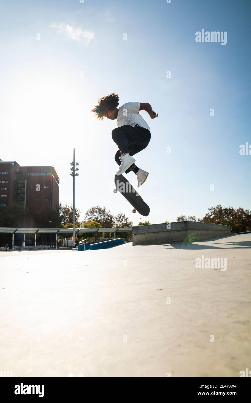 Lockiges Haar Mann tun Kickflip mit Skateboard an sonnigen Tag Stockfoto