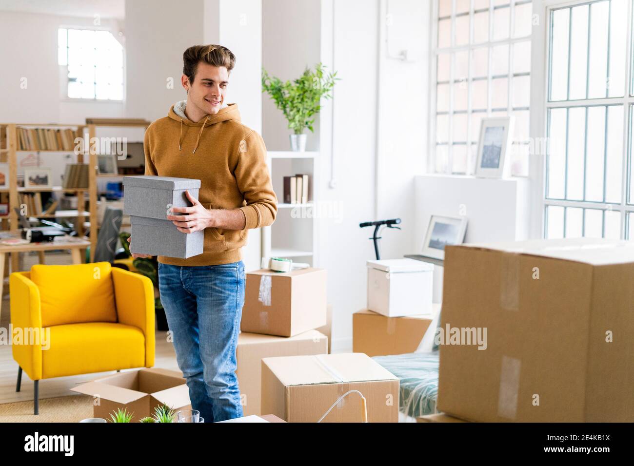 Lächelnder junger Mann, der Boxen hält, während er im neuen Loft steht Wohnung Stockfoto