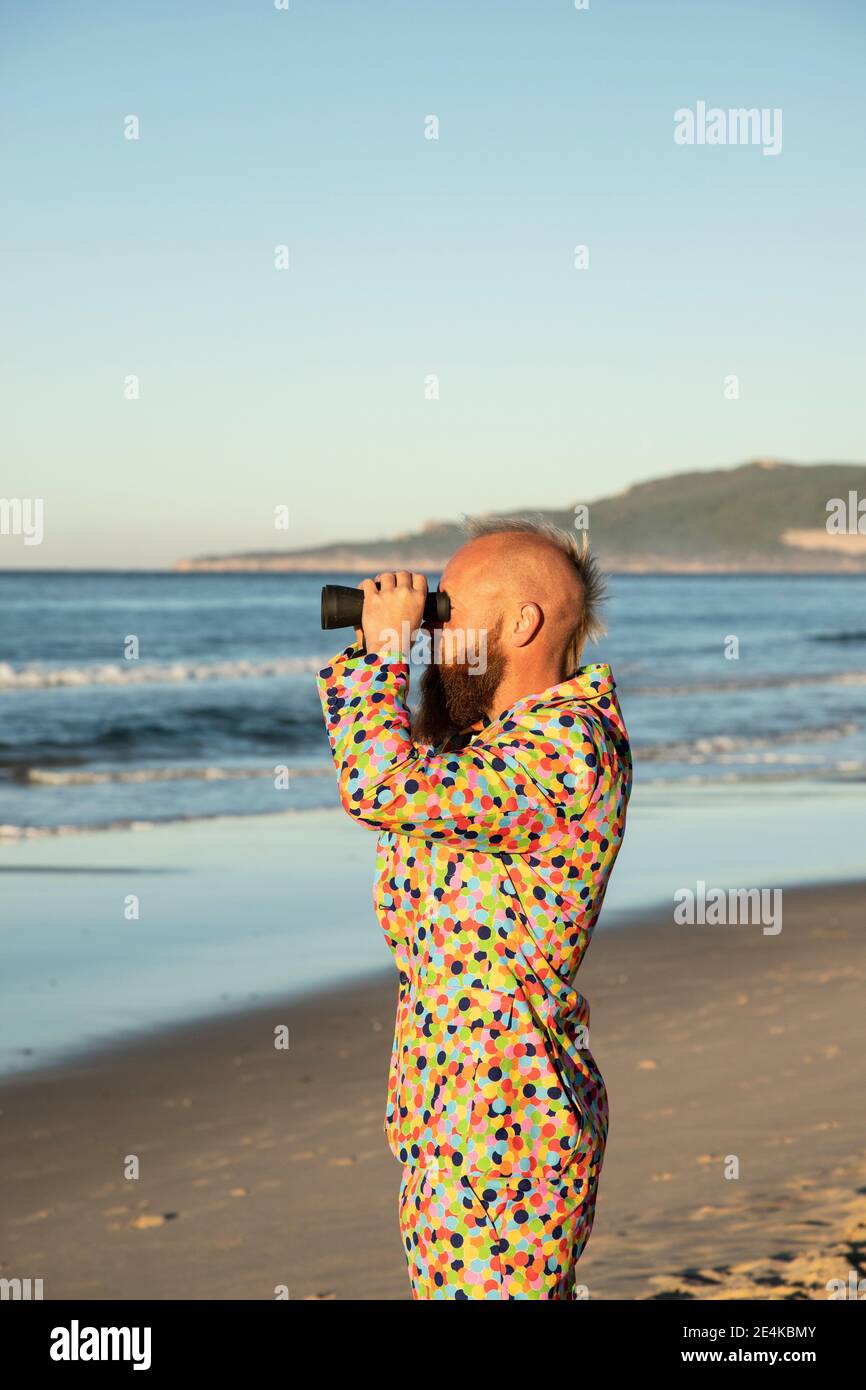 Mann im Anzug, der im Stehen durch das Fernglas auf das Meer schaut Strand Stockfoto