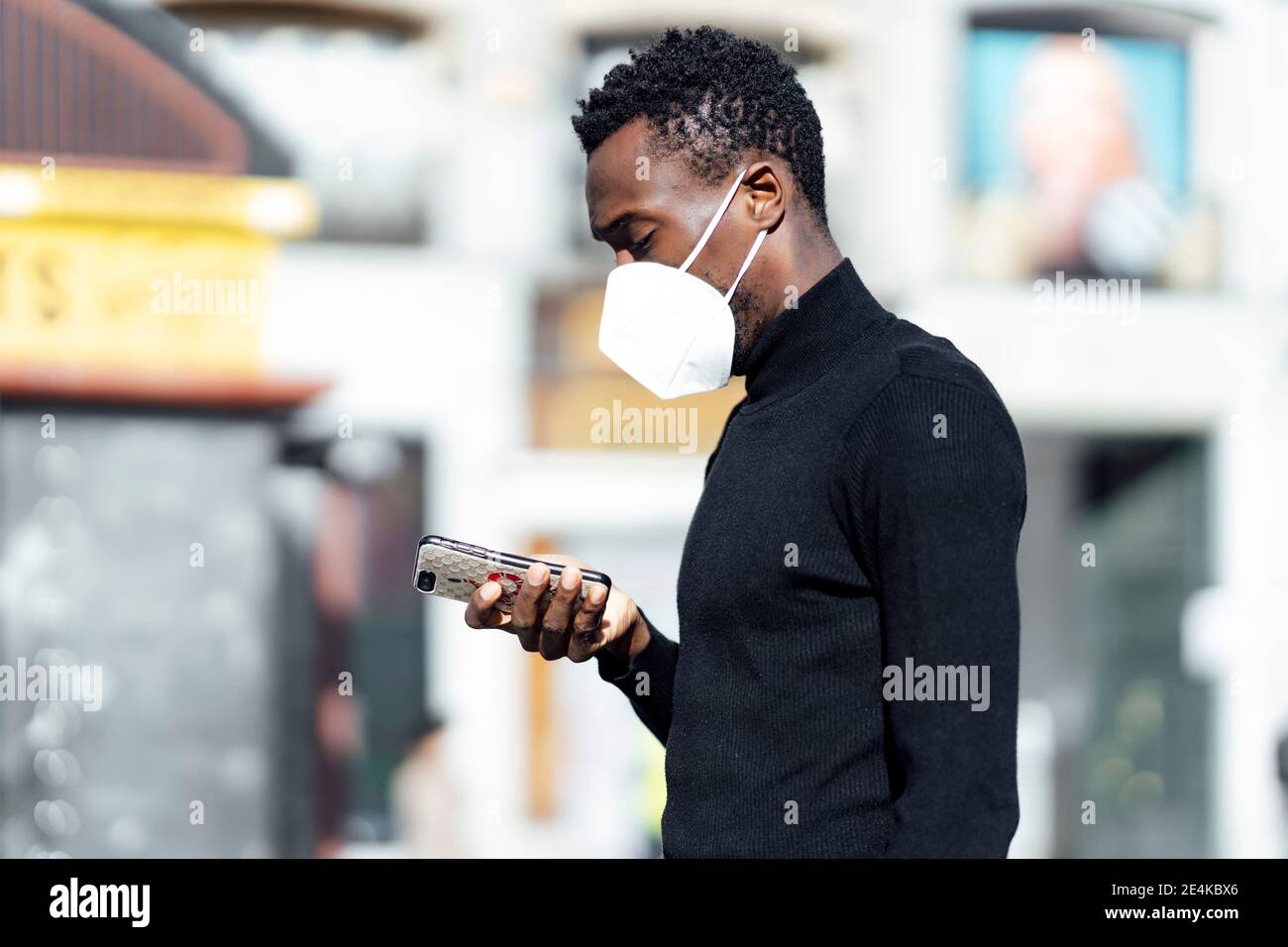 Junger Mann mit Gesichtsmaske und Mobiltelefon, während er im Freien steht Stockfoto