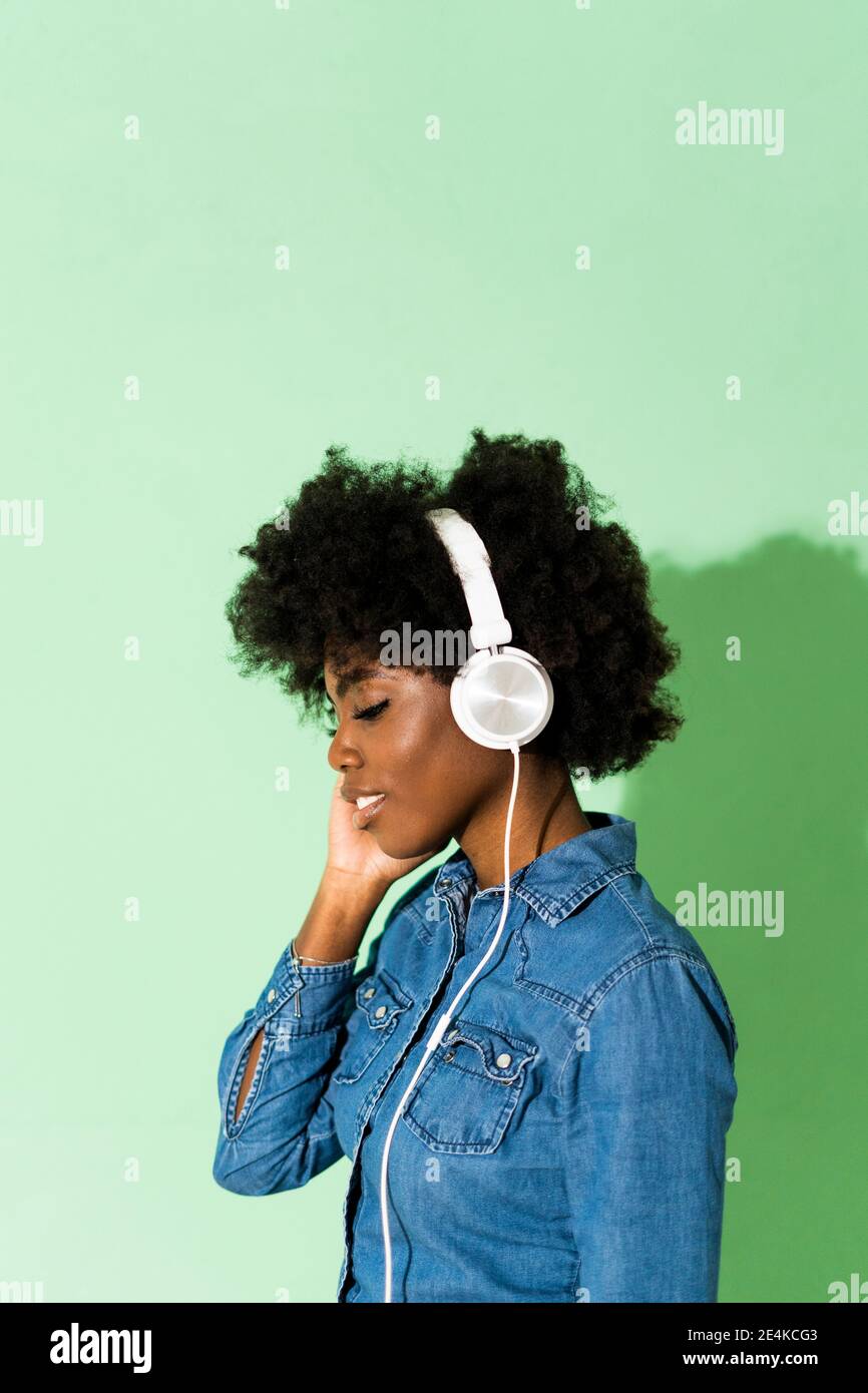 Junge Frau mit Kopfhörern, die vor grünem Hintergrund stehen Stockfoto