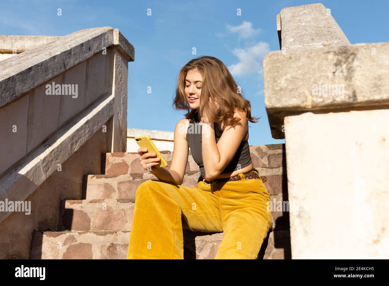 Junge Frau sitzt in Steinstufen im Freien, Blick auf Smartphone Stockfoto