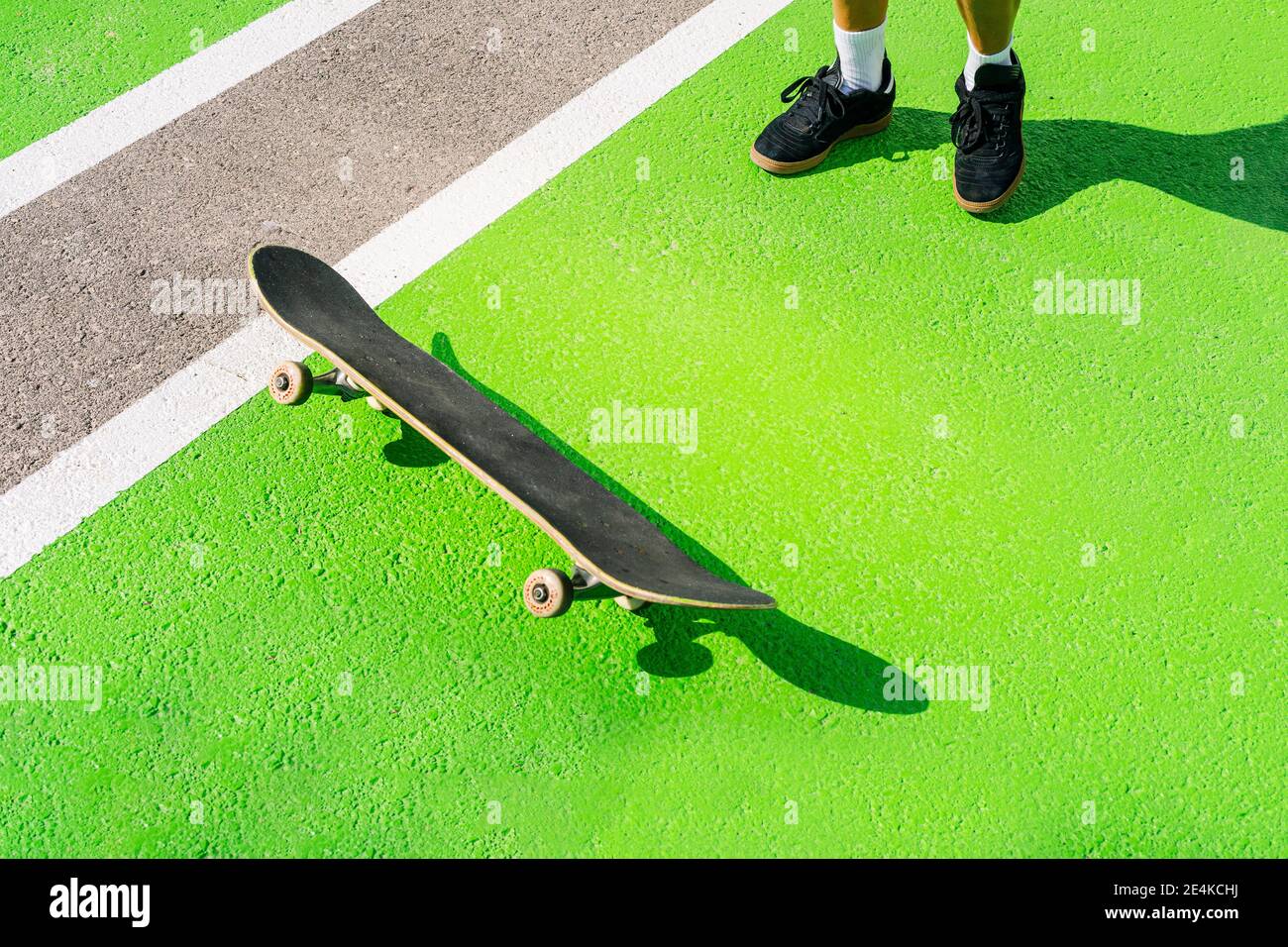 Füße einer erwachsenen Frau, die vor dem Skateboard steht und auf grüner Oberfläche liegt Stockfoto