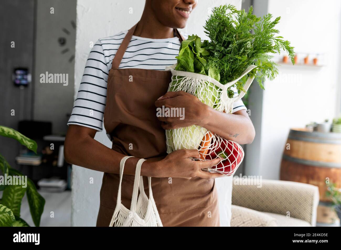 Hübsche Frau in Schürze, die Netz mit frischem Gemüse trägt Stockfoto