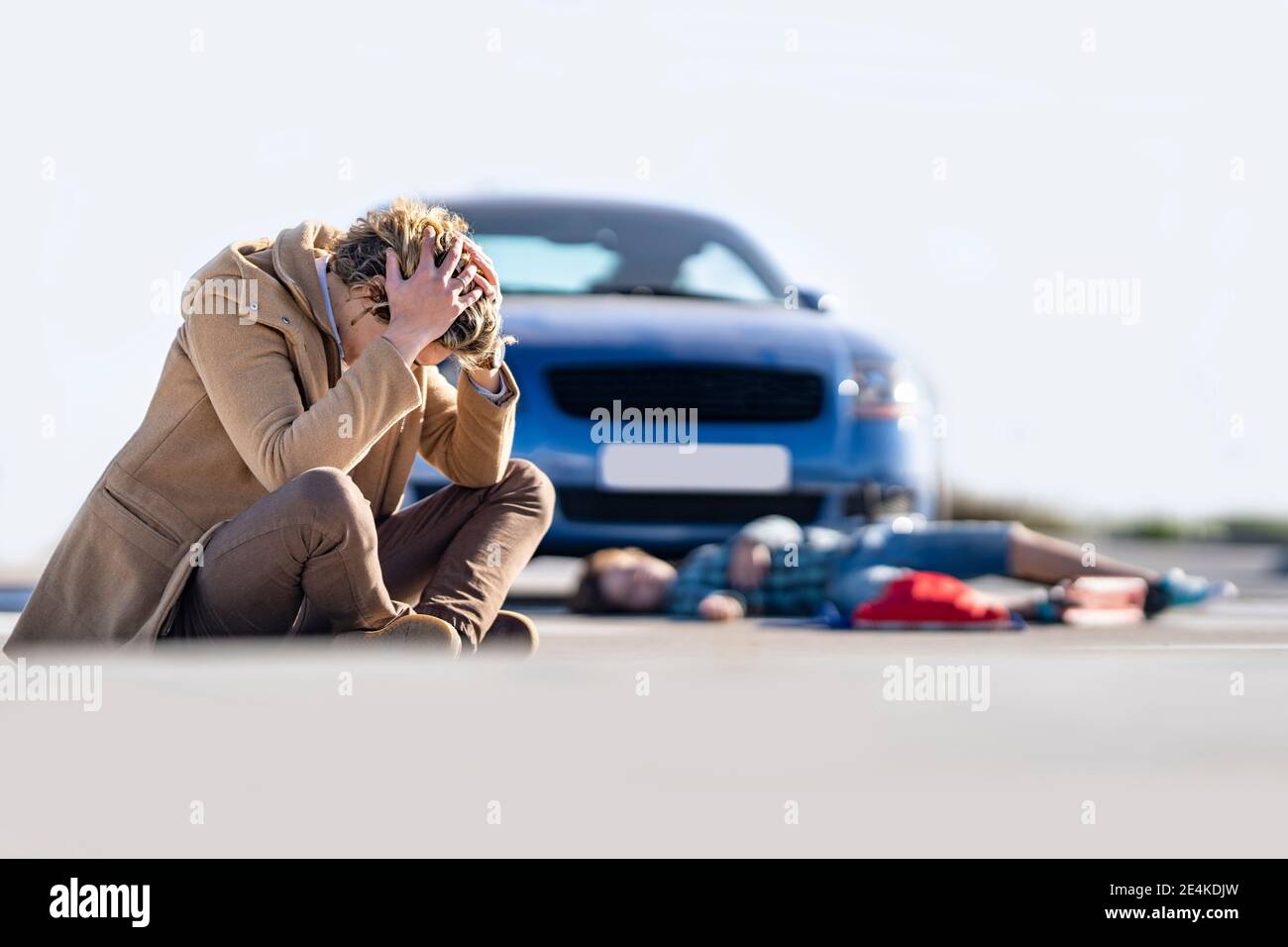 Verzweifelter junger Mann auf dem Boden mit Jungen im Hintergrund sitzen Mit dem Auto nach einem Unfall liegen Stockfoto