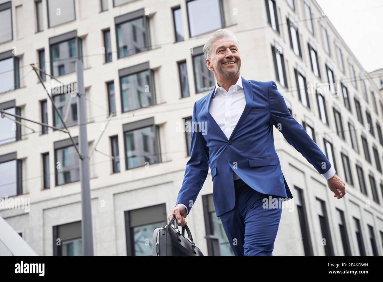 Lächelnder männlicher Unternehmer mit Tasche, die gegen das Gebäude läuft Stadt Stockfoto