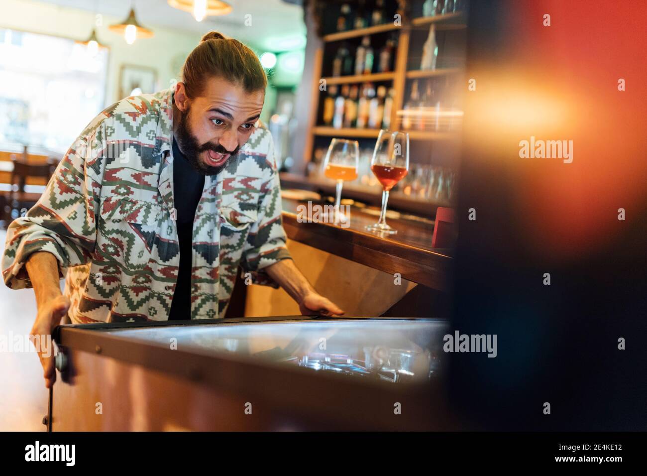 Fröhlicher bärtiger Mann spielt Flipper in der Bar Stockfoto