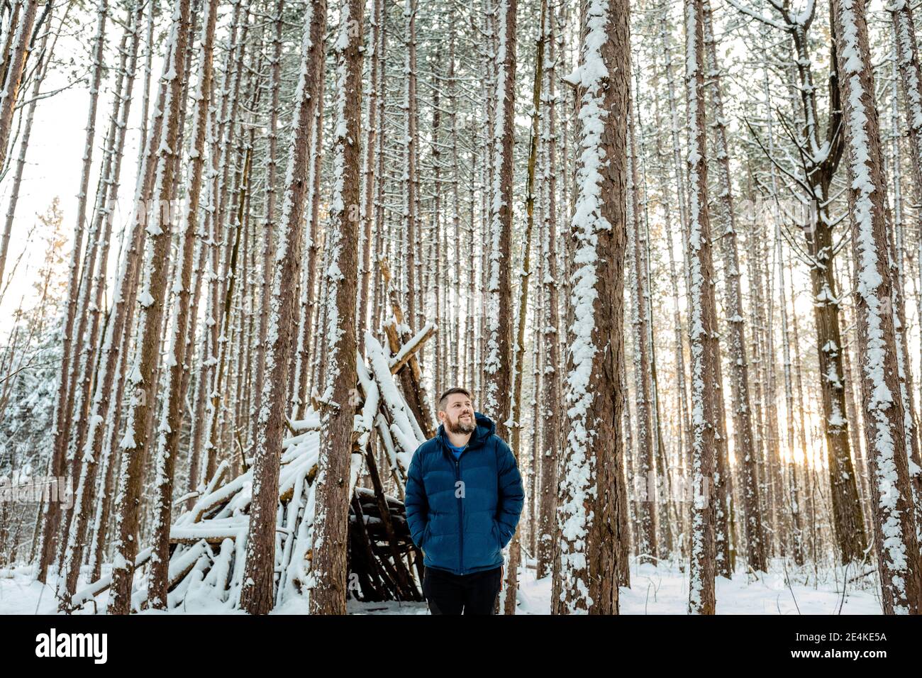 Mann schaut weg, während er im Wald gegen ein Holzzelt steht Stockfoto