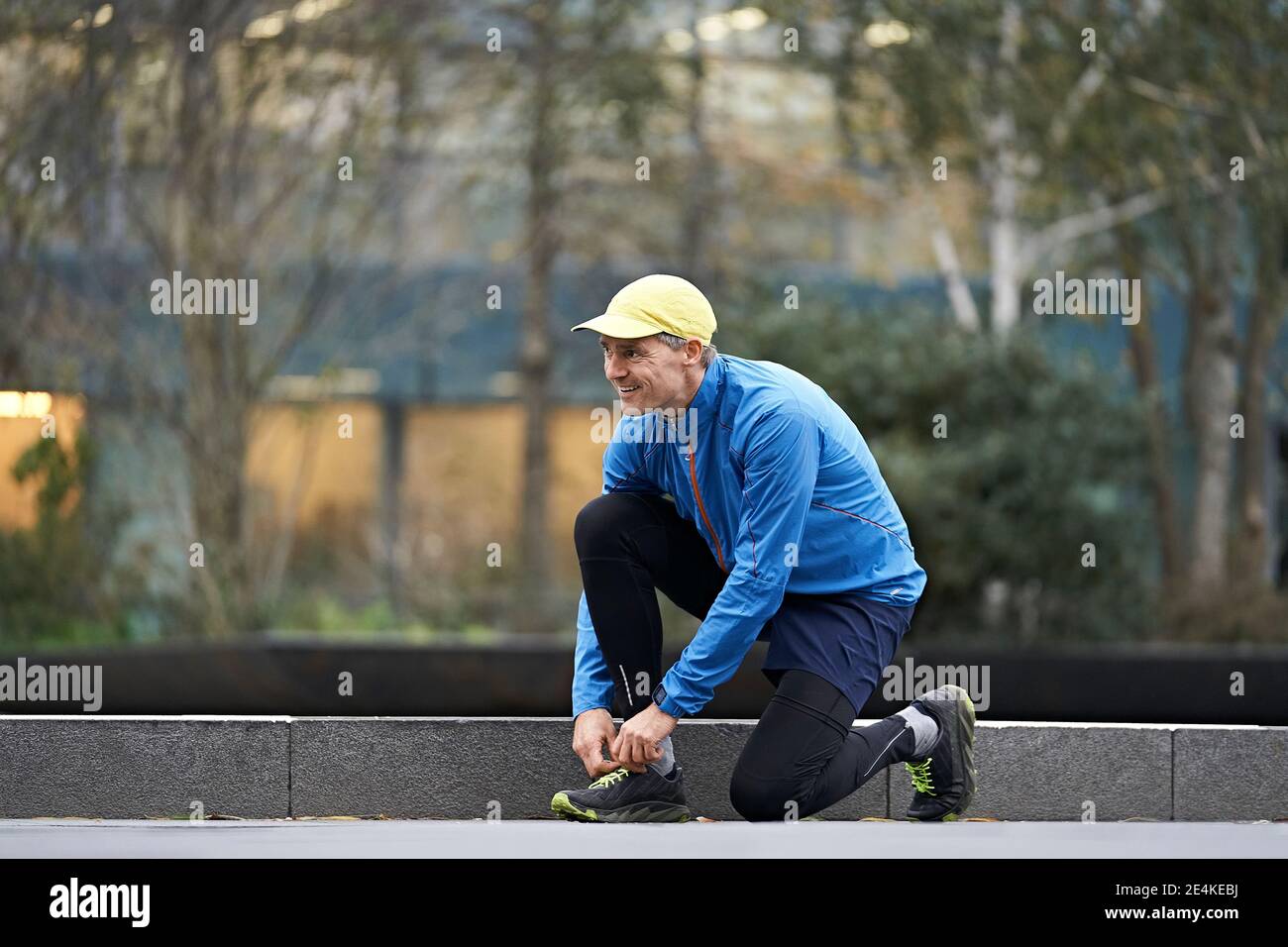 Lächelnder reifer Mann bindet Schnürsenkel auf Fußpfad beim Training Stockfoto